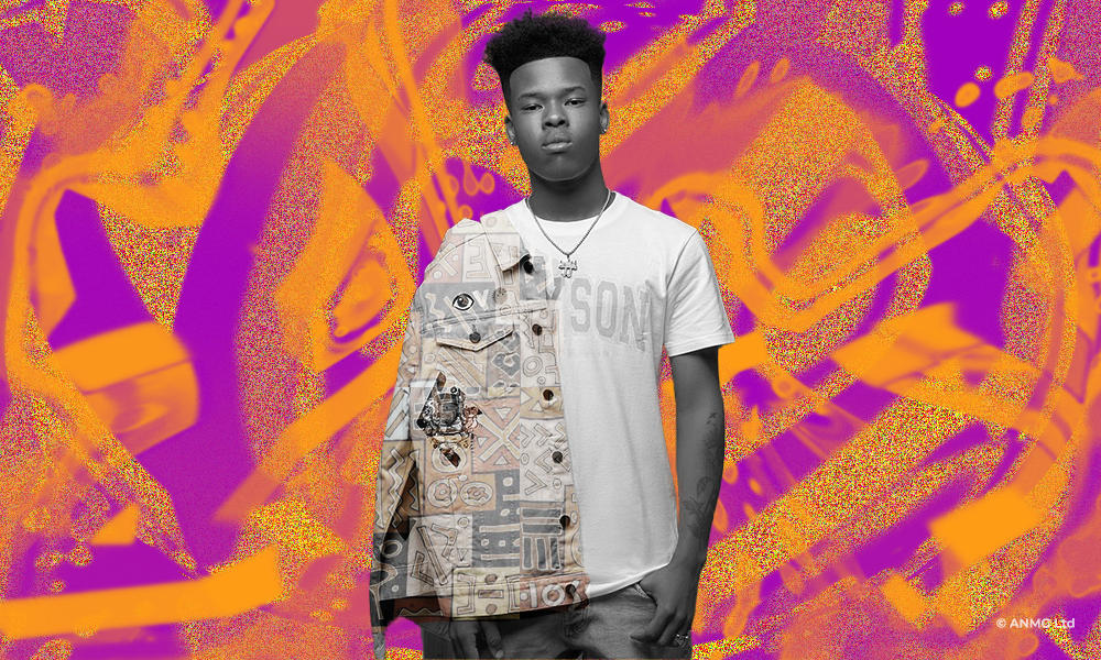 Nasty C standing in a jacket overlayed over his tshirt, in a necklace 